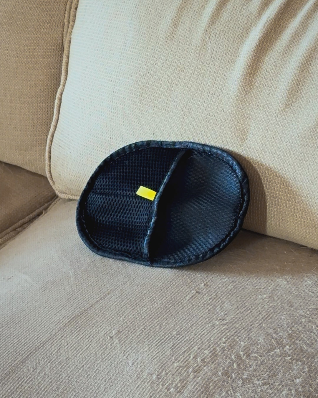 PawGroom furniture mitt on a beige sofa — mesh side with yellow tab